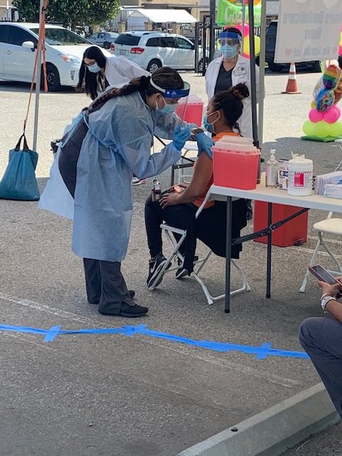 Female medical professional administering a shot to patient outside under tent.